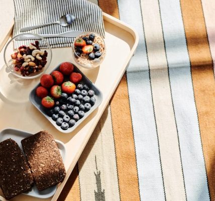 Top view of a healthy breakfast tray with fruits, bread, and juice on a striped tablecloth.