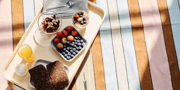 Top view of a healthy breakfast tray with fruits, bread, and juice on a striped tablecloth.